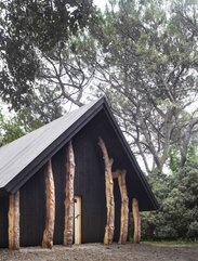 Eine kleine Kapelle aus dunklem Holz umgeben von Bäumen | © Alessandra Chemollo