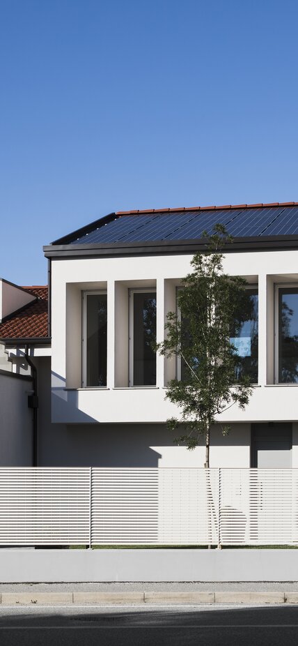 Un edificio residenziale a due piani con un'ampia fila di finestre al piano superiore e un impianto fotovoltaico sul tetto | © Davide Perbellini