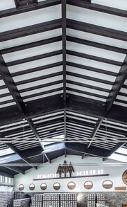 The wooden roof structure of a large production hall with dark painted glulam beams | © Benjamin Pfitscher