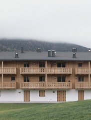 Edificio a tre piani con facciata intonacata al piano terra e scuri in legno, i due piani superiori e i balconi sono in legno non trattato | © Davide Perbellini