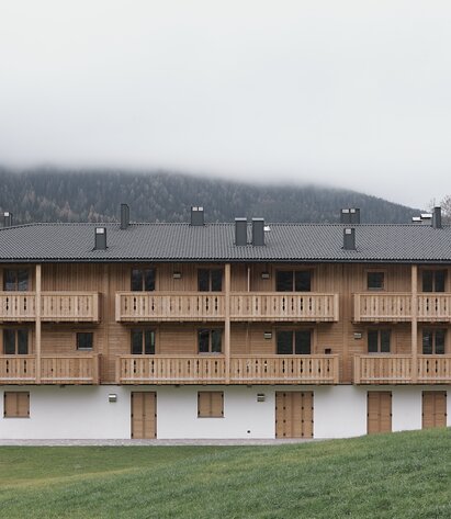 Ein dreistöckiges Gebäude mit einer verputzten Fasssade im Erdgeschoss und Fensterläden aus Holz, die zwei Obergeschosse und die Balkone sind aus naturbelassenem Holz | © Davide Perbellini