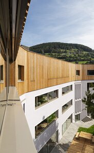 Ein Schulgebäude, auf den drei verputzten Untergeschossen steht ein vierter Stock mit einer vertikal laufenden Verkleidung aus Lärchenholz | © Samuel Holzner