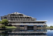 Ein großes Gebäude mit einer Fassade aus dunklem Holz, im Vordergrund ein Freischwimmbad | © Florian Andergassen